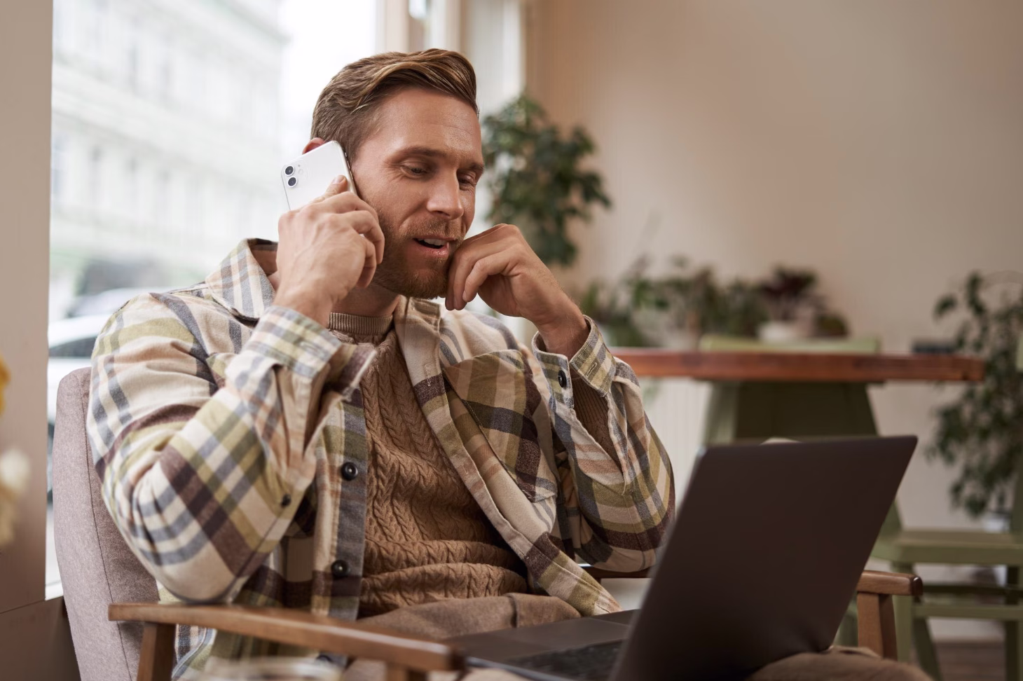 painter following up with a facebook lead with his IPhone from a cafe, wearing flannel on using a laptop